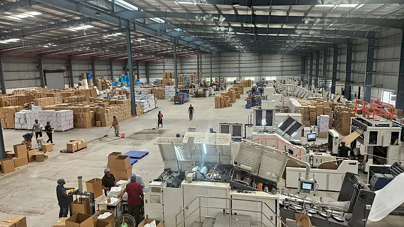 J K Industries production floor: rows of paper bag making machines, with packed cartons and paper reels stacked behind